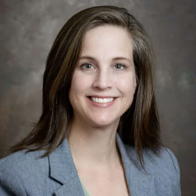 Headshot of a smiling white woman with long brown hair and a gray blazer