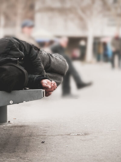 Homeless person sleeping on a bench in a city