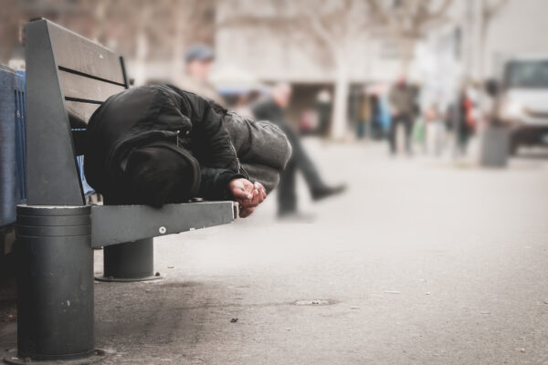 Homeless person sleeping on a bench in a city