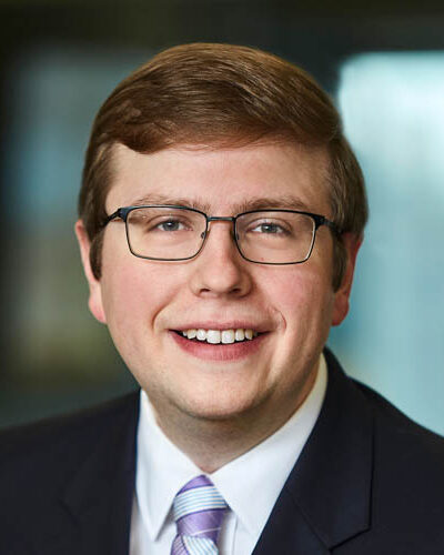 A portrait headshot of David Fry, wearing a suit and a purple and blue striped tie.