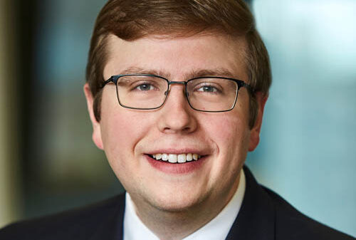 A portrait headshot of David Fry, wearing a suit and a purple and blue striped tie.