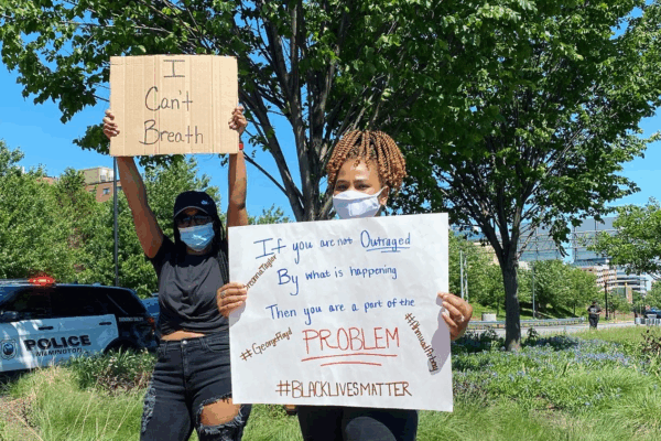 Two women holding signs at police violence protest, standing in front of Wilmington Police Department SUV on Martin Luther King Blvd in Wilmington