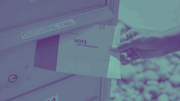 A person's hand inserting a mail ballot into an outgoing mail box.
