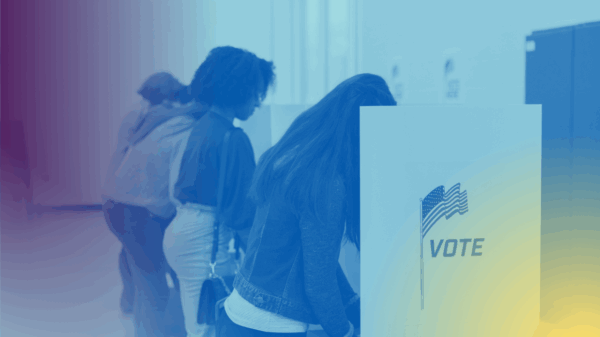 Voters fill out their ballots at voting cubicles in a school gym.