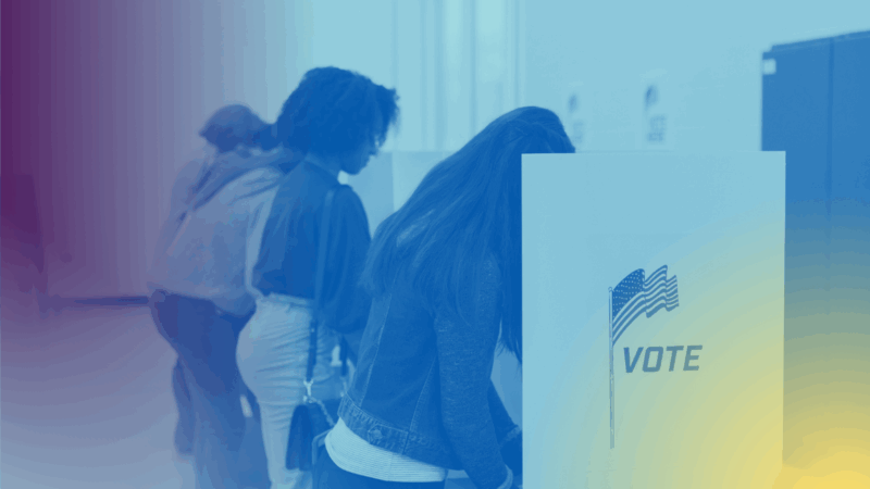 Voters fill out their ballots at voting cubicles in a school gym.