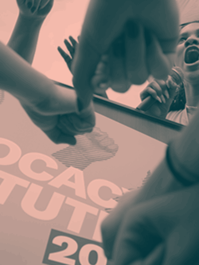 A photo of an activist yelling into a microphone, surrounded by other activists.