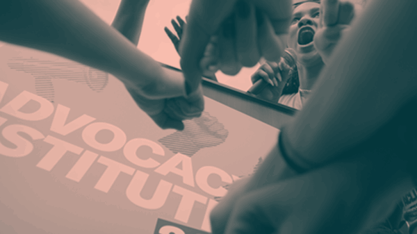 A photo of an activist yelling into a microphone, surrounded by other activists.