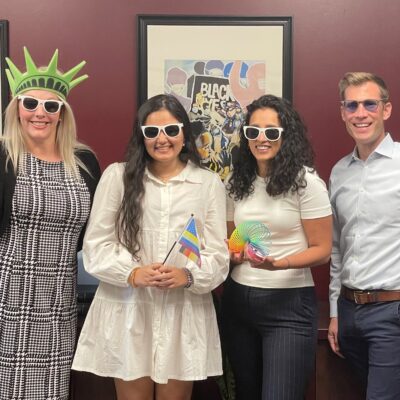 Photo of ACLU Delaware's legal team: Katie, Jasmine, Charmi, and Dwayne. They are wearing sunglasses and holding pride and patriotic swag.