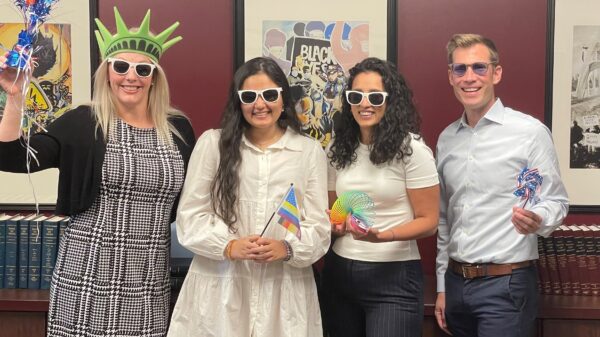 Photo of ACLU Delaware's legal team: Katie, Jasmine, Charmi, and Dwayne. They are wearing sunglasses and holding pride and patriotic swag.