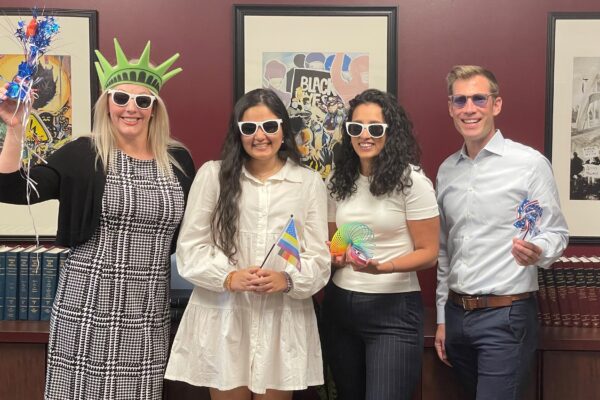 Photo of ACLU Delaware's legal team: Katie, Jasmine, Charmi, and Dwayne. They are wearing sunglasses and holding pride and patriotic swag.