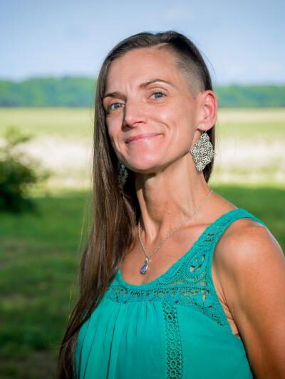 A headshot of Shannon Shapter standing outside, wearing a teal-aqua green top with her long brown hair pulled to one side.