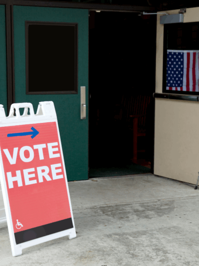 Image of building with door open, with a "vote here" sign near the open door.