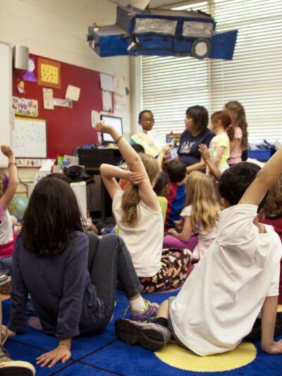 Students sitting on classroom floor listening to teacher.