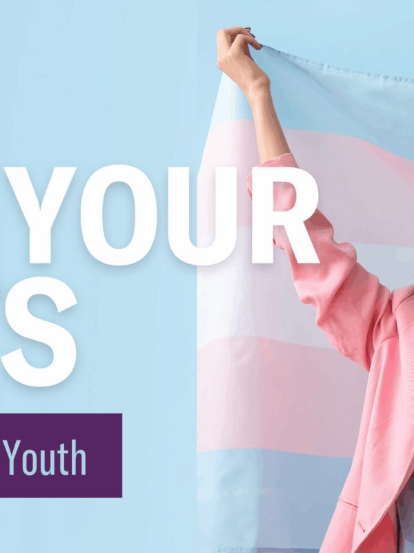 Young smiling person with green highlights and makeup holds up a trans rights flag with a joyous expression