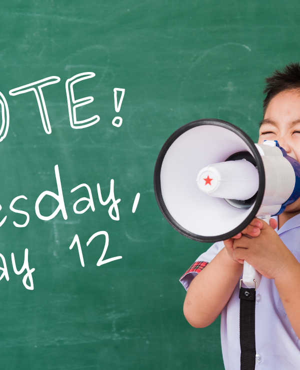 A kid with a megaphone stands in front of a chalkboard that reads "Vote! Tuesday, May 12"
