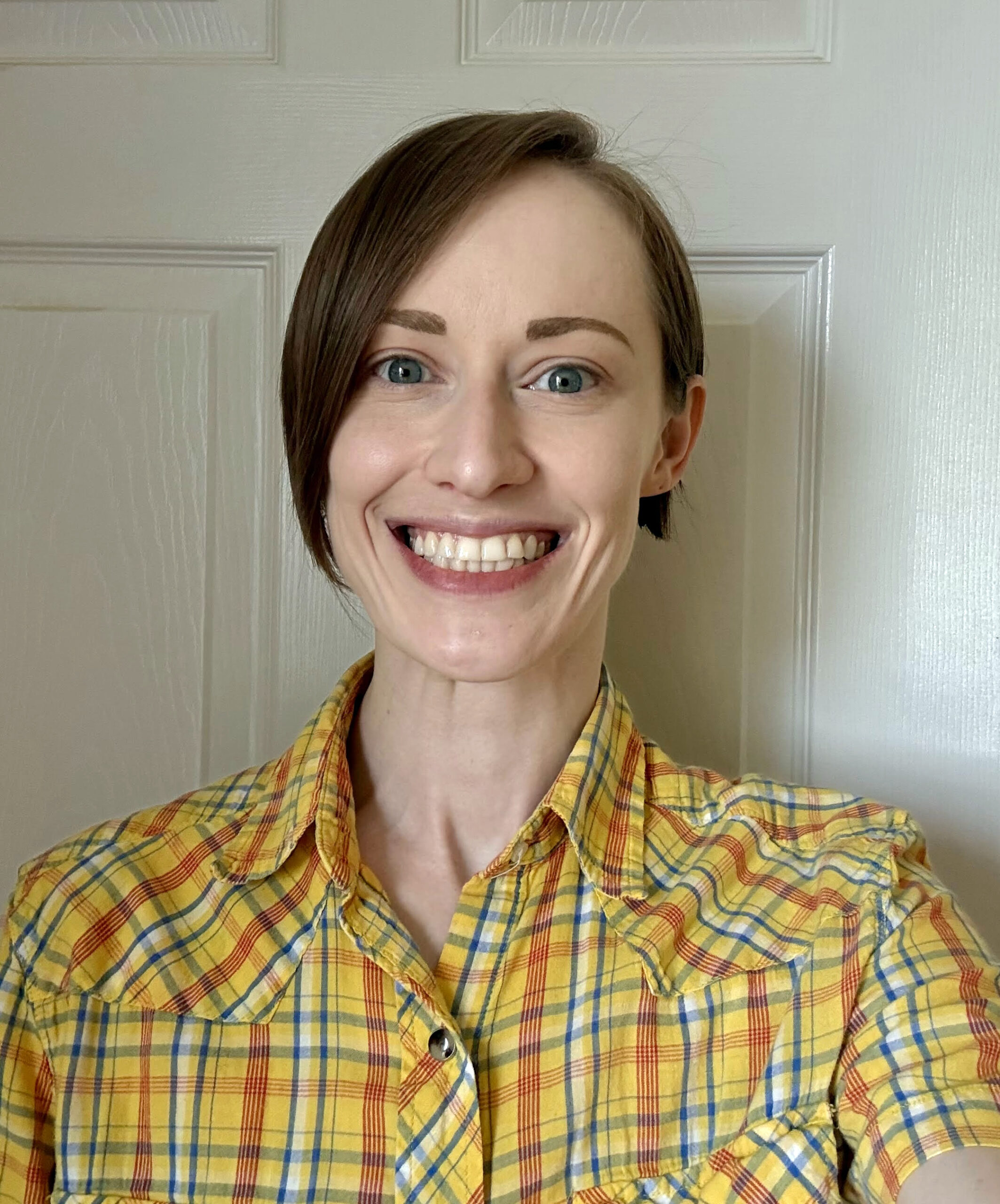 Jac Cichocki wearing a yellow plaid shirt and smiling in front of a white background