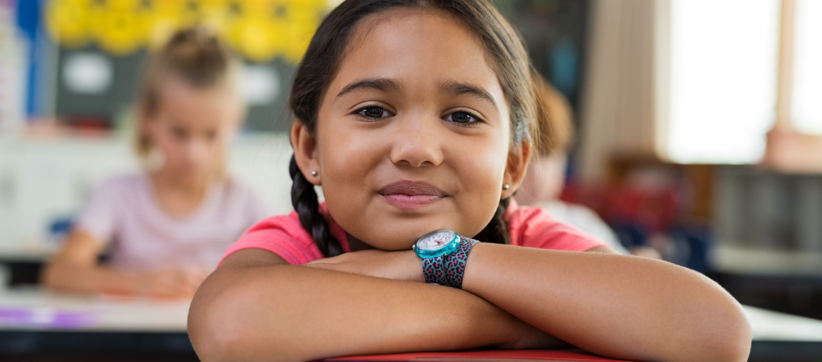 Girl in classroom with arms crossed on desk over books