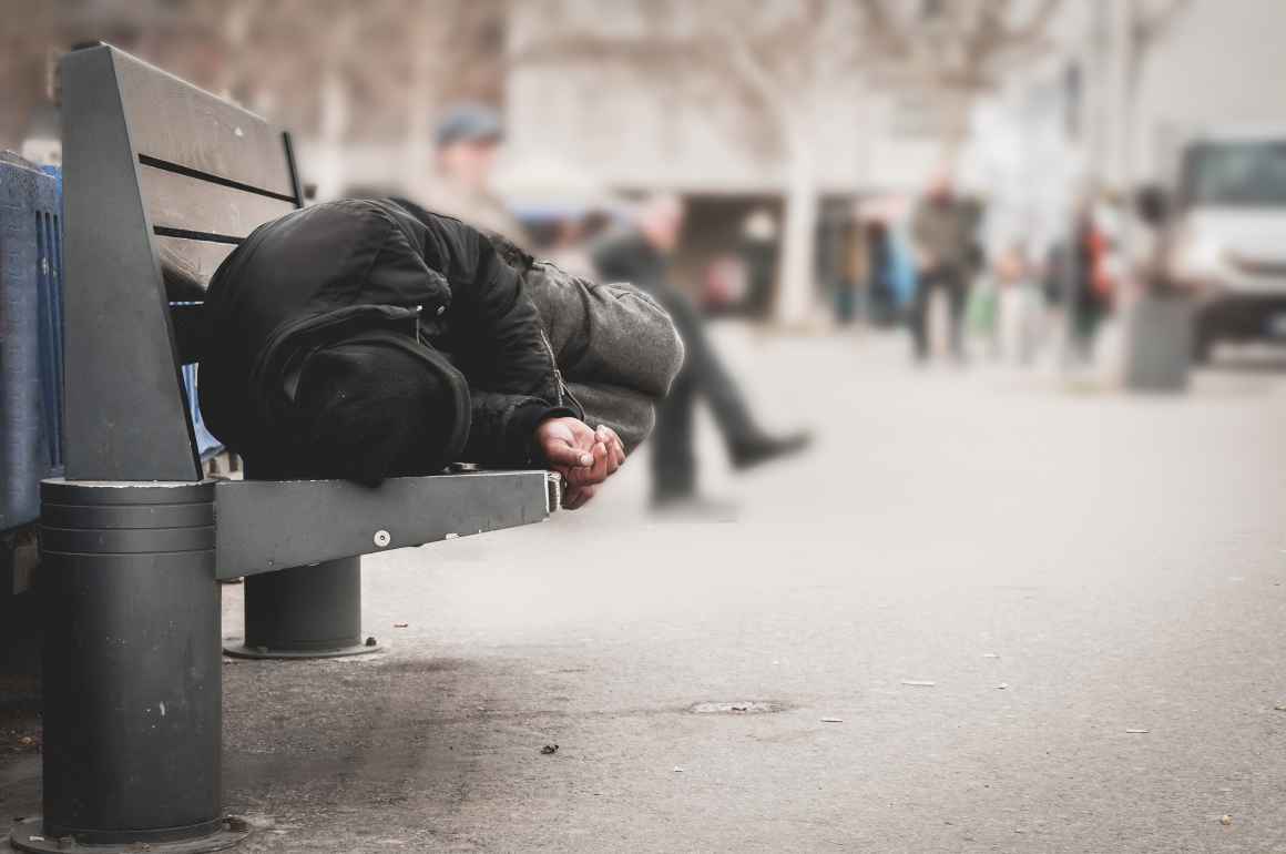Homeless person sleeping on a bench in a city
