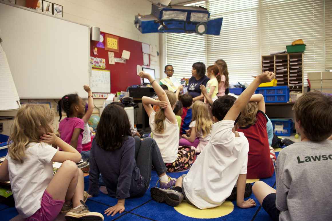 Students sitting on classroom floor listening to teacher.