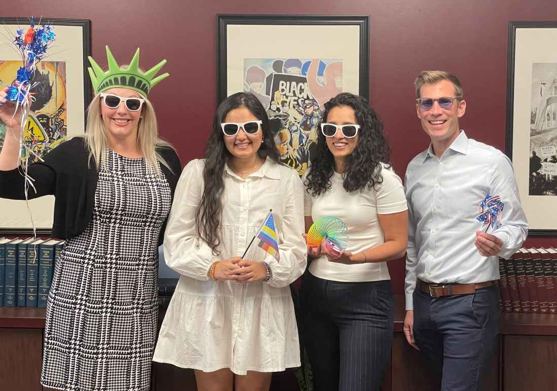 Photo of ACLU Delaware's legal team: Katie, Jasmine, Charmi, and Dwayne. They are wearing sunglasses and holding pride and patriotic swag.