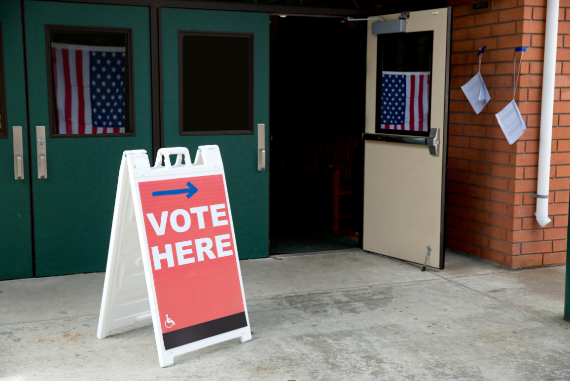 Image of building with door open, with a "vote here" sign near the open door.