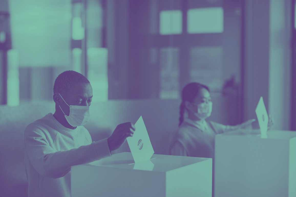 Photo of two people wearing masks and dropping ballots in ballot boxes.