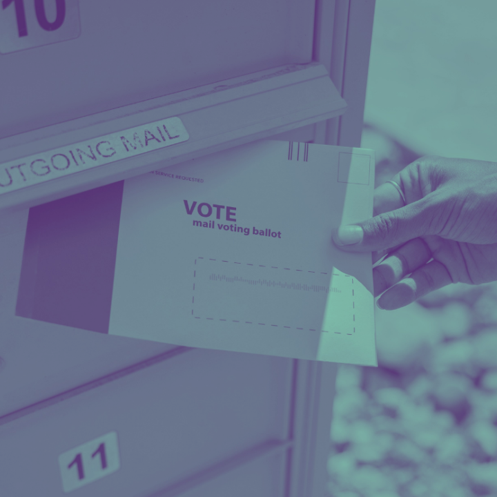 photograph of a person's hand putting a mail ballot in an "outgoing mail" mailbox.
