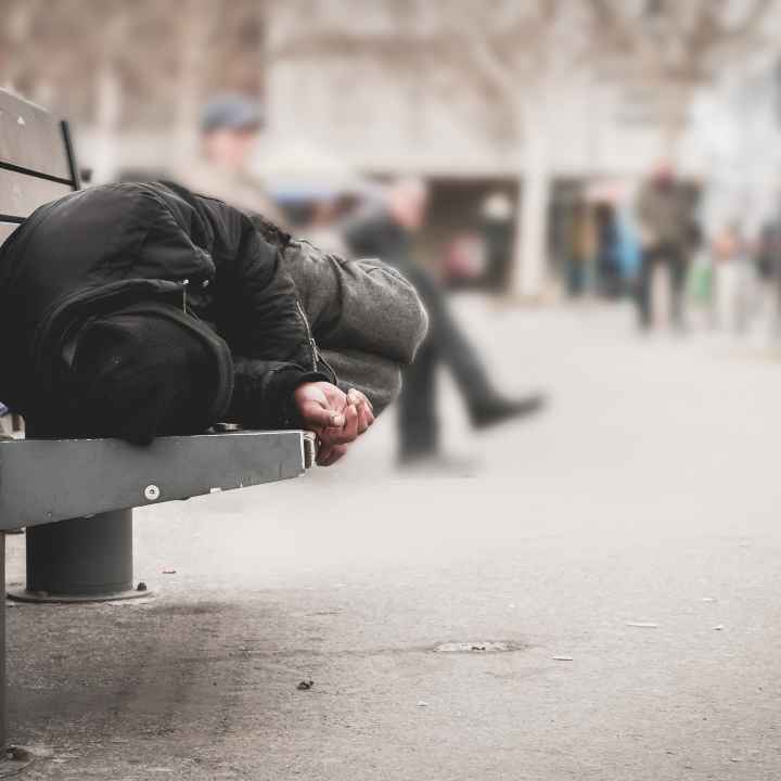 Homeless person sleeping on a bench in a city