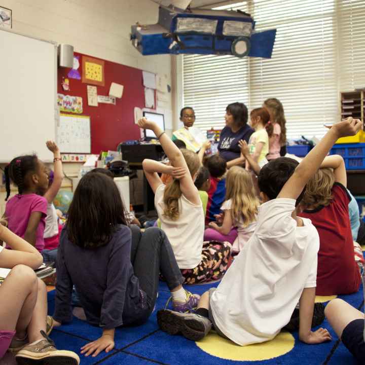 Students sitting on classroom floor listening to teacher.