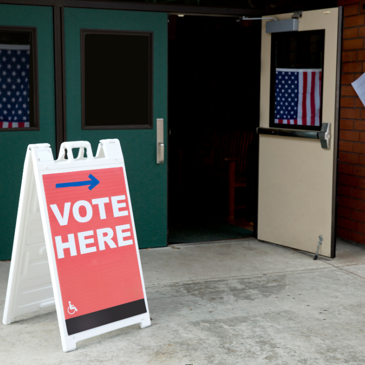 Image of building with door open, with a "vote here" sign near the open door.