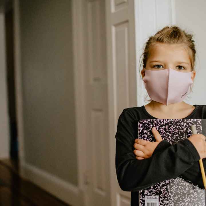Child holding notebook with face mask on