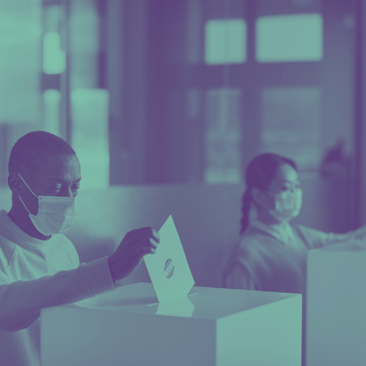 Photo of two people wearing masks and dropping ballots in ballot boxes.