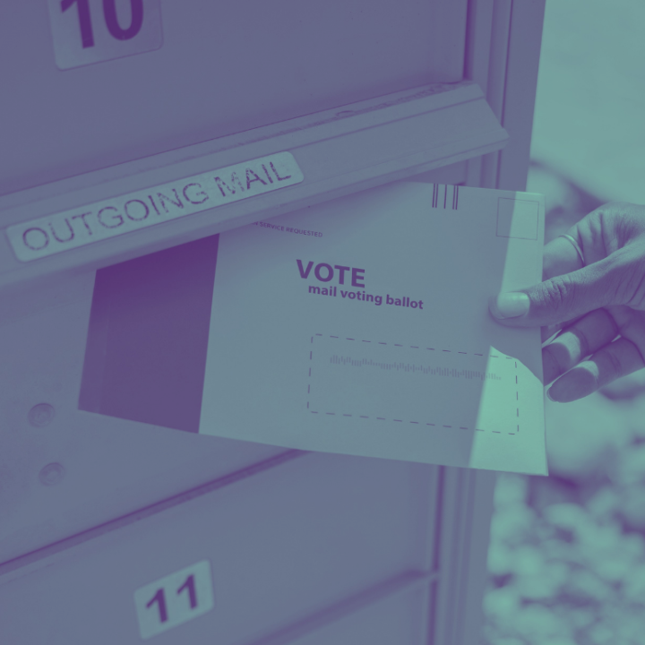 A person's hand inserting a mail ballot into an outgoing mail box.